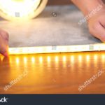 stock-photo-the-master-installs-a-luminous-led-strip-close-up-hands-stick-tape-on-a-wooden-surface-1729759978.jpg